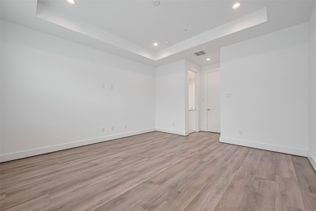 unfurnished room with baseboards, light wood-type flooring, a tray ceiling, and recessed lighting