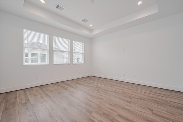 spare room with a raised ceiling, light wood-type flooring, and visible vents