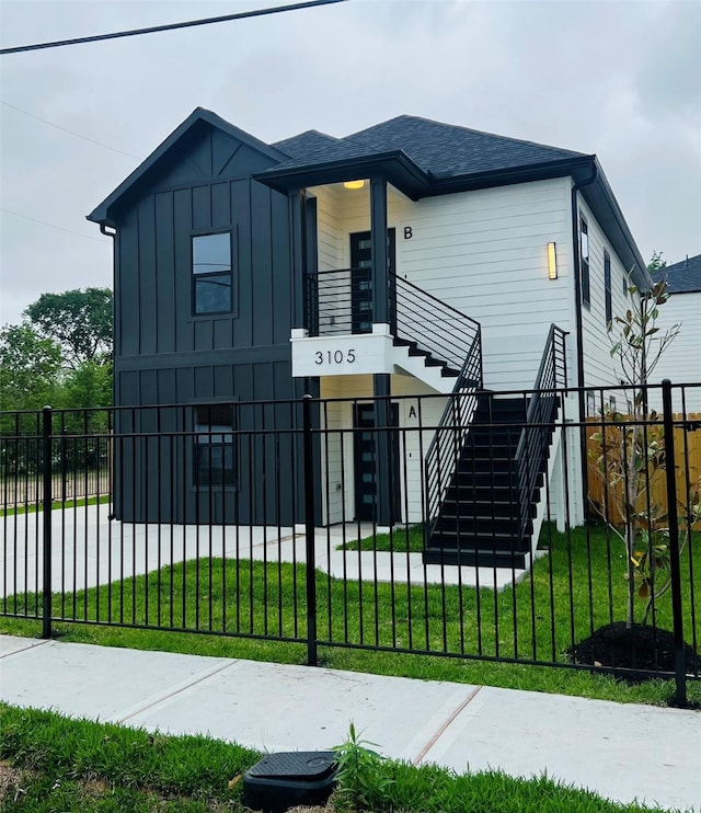 view of front of home featuring stairs, a shingled roof, a fenced front yard, a front lawn, and board and batten siding