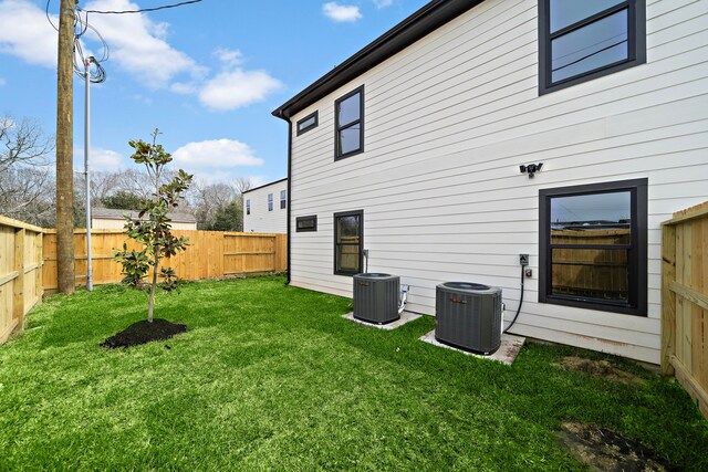 back of house with central AC unit, a fenced backyard, and a yard