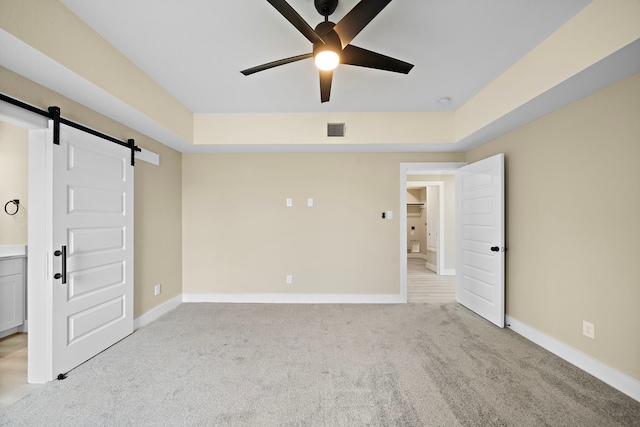 spare room with ceiling fan, visible vents, light colored carpet, a barn door, and baseboards