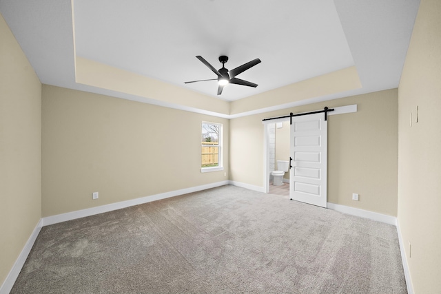 unfurnished bedroom with carpet floors, a barn door, and a tray ceiling