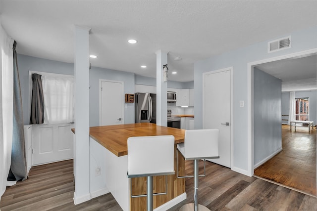 386 N Post Oak Ln, Houston, TX 77024 - kitchen with stainless steel appliances, butcher block counters, white cabinets, dark wood finished floors, and baseboards
