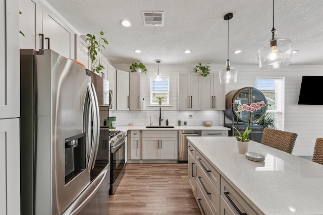 kitchen featuring stainless steel appliances, a textured ceiling, a sink, and wood finished floors
