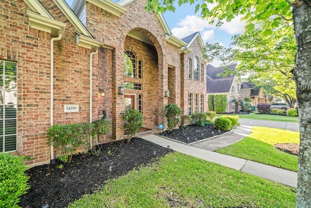 entrance to property featuring a lawn and brick siding
