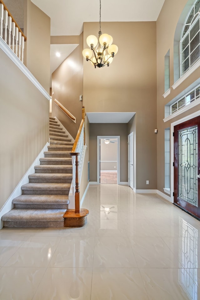 foyer featuring stairway, baseboards, an inviting chandelier, and a towering ceiling