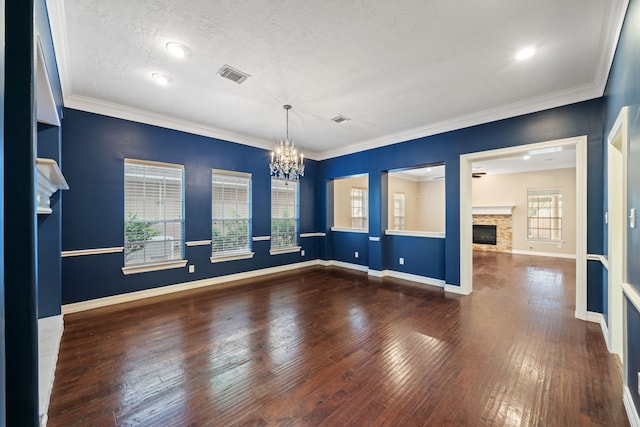 spare room featuring a stone fireplace, visible vents, baseboards, wood-type flooring, and an inviting chandelier