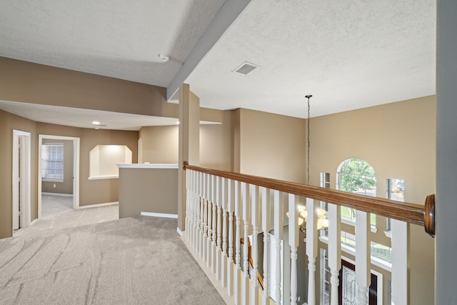 corridor with visible vents, baseboards, a textured ceiling, carpet flooring, and an upstairs landing