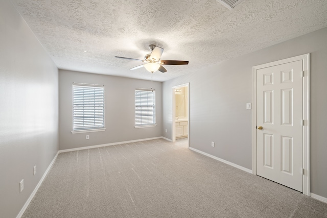 unfurnished bedroom with baseboards, connected bathroom, a textured ceiling, and light colored carpet