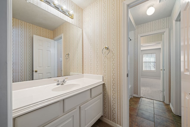 bathroom with baseboards, vanity, and wallpapered walls