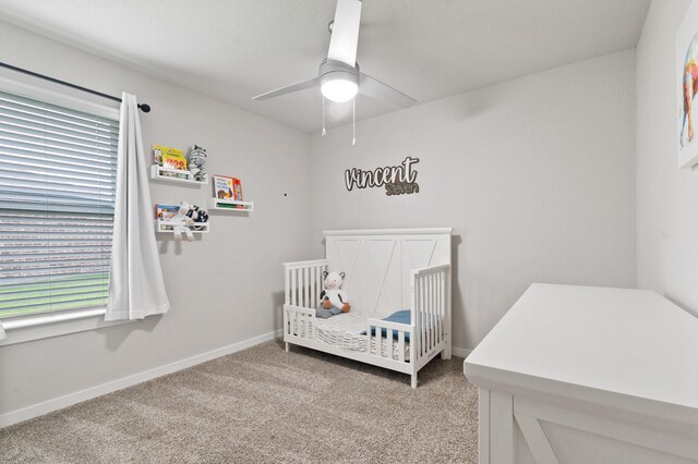 carpeted bedroom featuring a ceiling fan, baseboards, a crib, and multiple windows