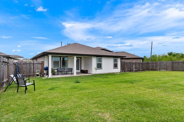 rear view of property with a lawn, roof with shingles, a fenced backyard, and a patio area