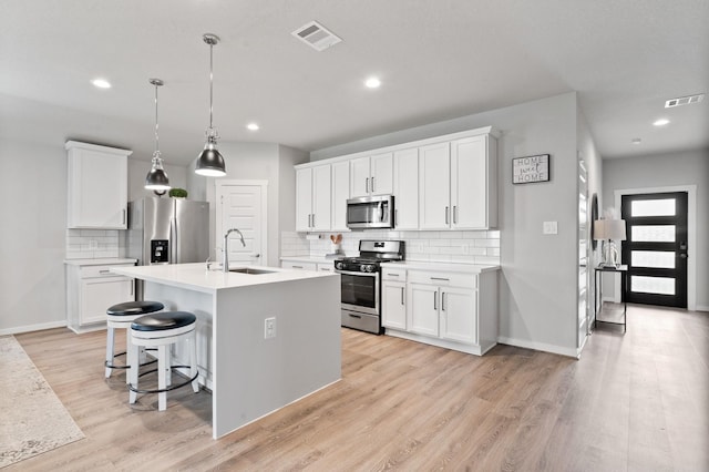 kitchen featuring a center island with sink, a sink, light wood-style flooring, backsplash, and stainless steel appliances
