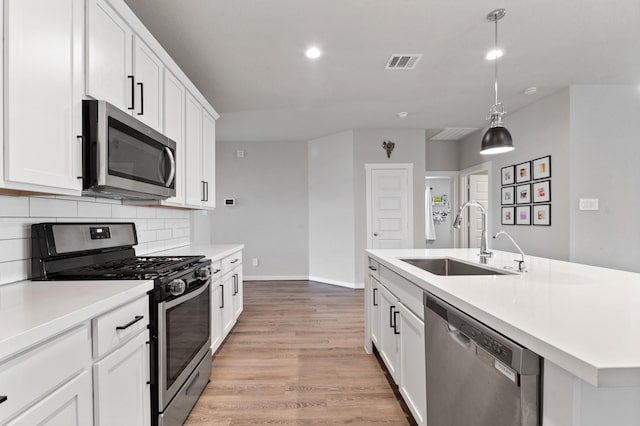 kitchen with a sink, light countertops, light wood-style flooring, stainless steel appliances, and decorative backsplash