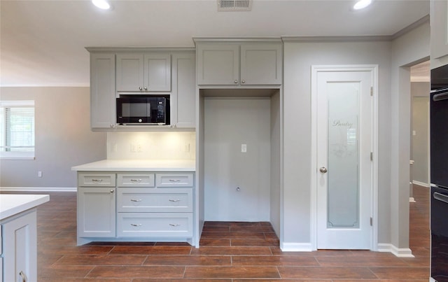kitchen with wood finish floors, black microwave, gray cabinets, baseboards, and ornamental molding