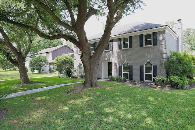 colonial home with brick siding, a front lawn, and a chimney