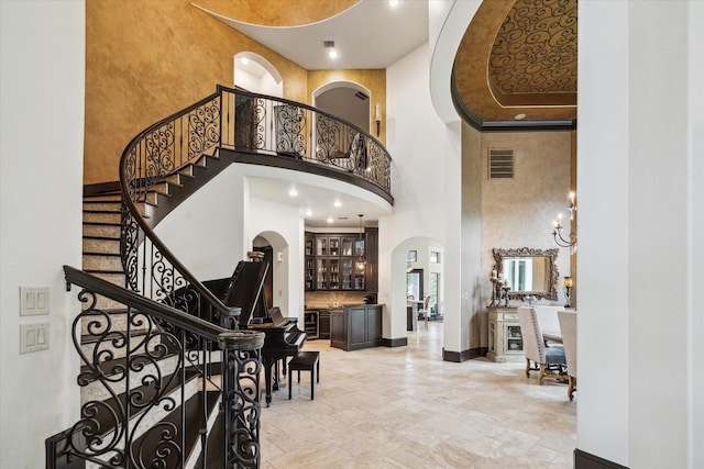 entrance foyer with visible vents, arched walkways, stairway, baseboards, and a high ceiling