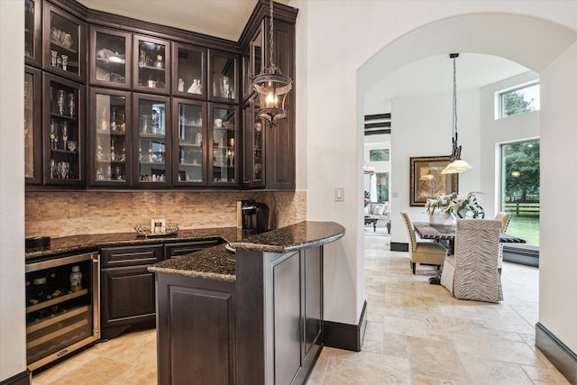 bar featuring stone tile flooring, decorative backsplash, beverage cooler, baseboards, and arched walkways