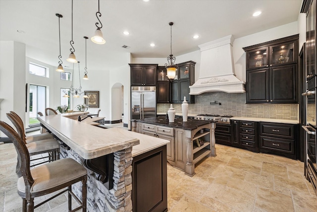 kitchen featuring decorative backsplash, appliances with stainless steel finishes, arched walkways, a spacious island, and custom exhaust hood