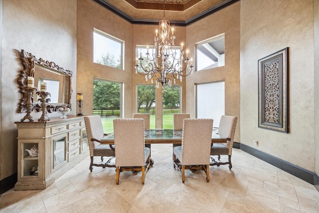dining room with an inviting chandelier, ornamental molding, stone tile flooring, and a towering ceiling