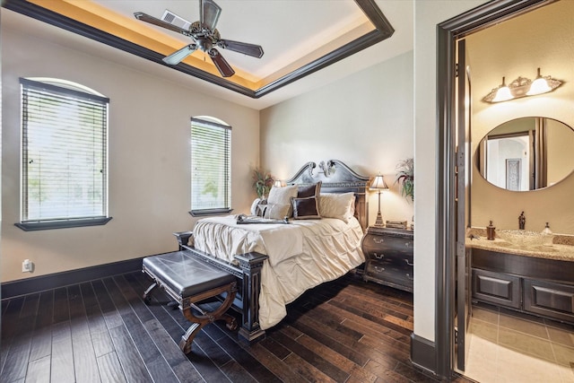 bedroom with ceiling fan, dark wood-style flooring, a raised ceiling, baseboards, and ensuite bathroom