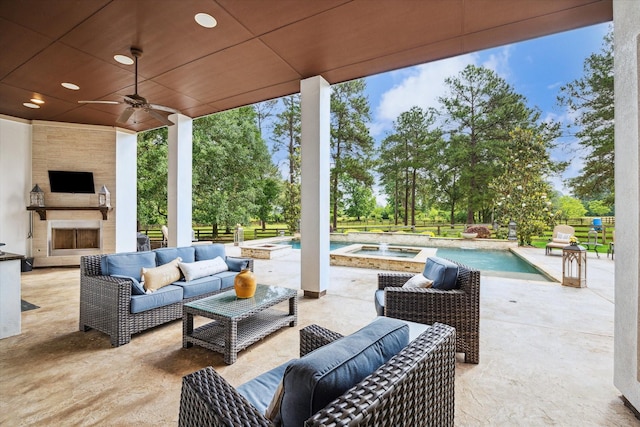 view of patio / terrace with fence, a ceiling fan, an outdoor living space with a fireplace, and a pool with connected hot tub