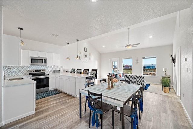 dining room featuring ceiling fan, a textured ceiling, visible vents, light wood finished floors, and lofted ceiling