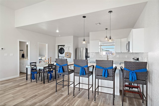 kitchen featuring appliances with stainless steel finishes, light wood-style floors, decorative backsplash, visible vents, and stacked washer and clothes dryer