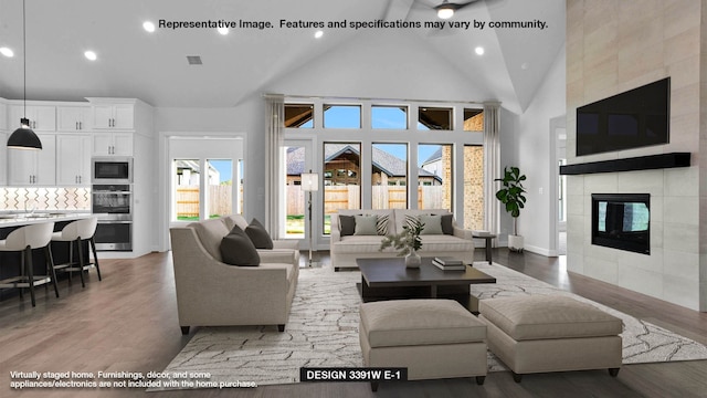 living room featuring light wood-type flooring, recessed lighting, high vaulted ceiling, and a tile fireplace