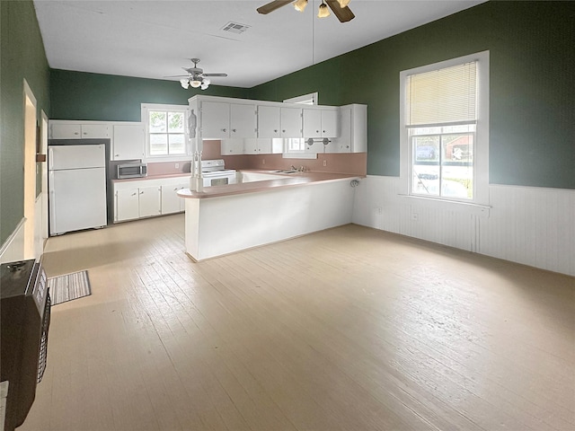 kitchen with a ceiling fan, visible vents, a wainscoted wall, a peninsula, and white appliances