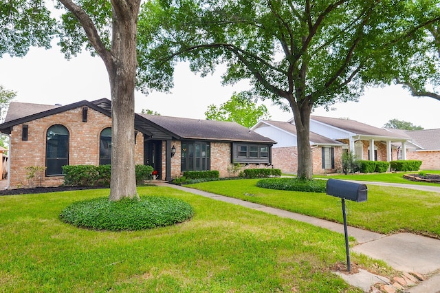 single story home featuring brick siding, a shingled roof, and a front yard