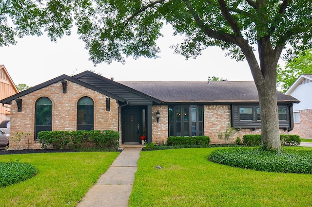 ranch-style house with roof with shingles, a front yard, and brick siding