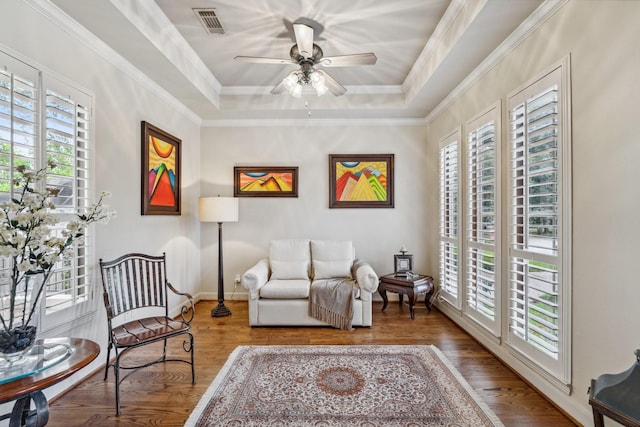 sitting room with visible vents, wood finished floors, baseboards, ceiling fan, and a tray ceiling
