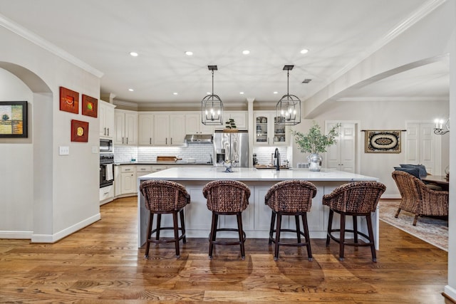 kitchen featuring arched walkways, stainless steel fridge with ice dispenser, under cabinet range hood, white cabinetry, and oven