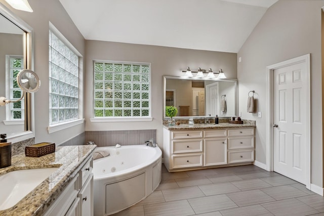 full bath with a sink, vaulted ceiling, a tub with jets, and two vanities