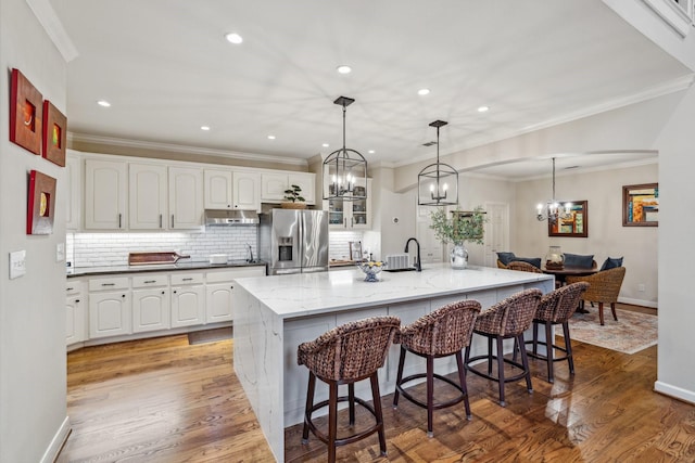 kitchen with a kitchen breakfast bar, stainless steel refrigerator with ice dispenser, white cabinets, an inviting chandelier, and under cabinet range hood