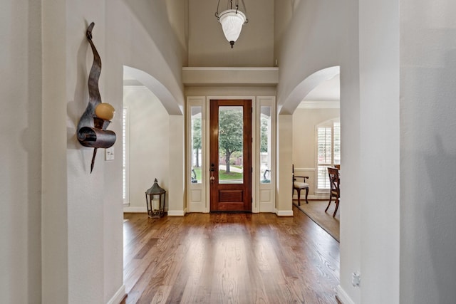 foyer featuring arched walkways, baseboards, wood finished floors, and a high ceiling