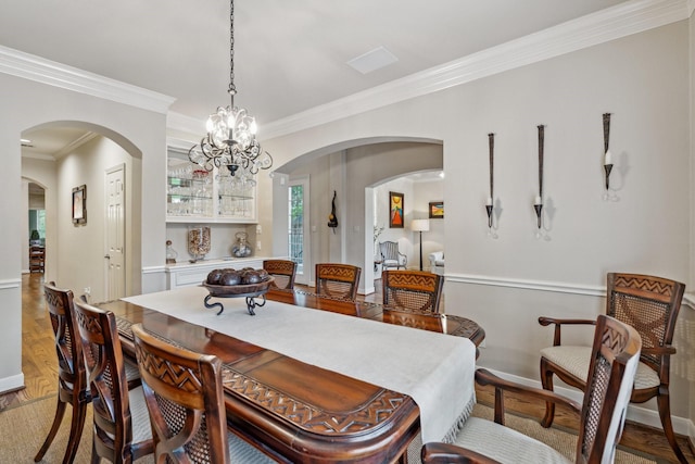 dining room featuring crown molding, an inviting chandelier, light wood finished floors, arched walkways, and baseboards