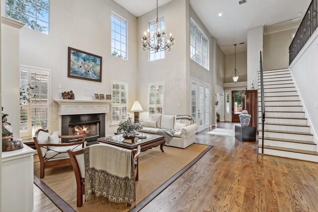 living area featuring a lit fireplace, a towering ceiling, wood finished floors, a notable chandelier, and stairs