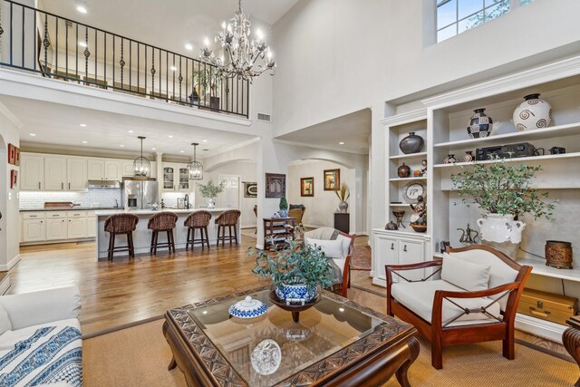 living room featuring arched walkways, light wood-style floors, an inviting chandelier, and a towering ceiling