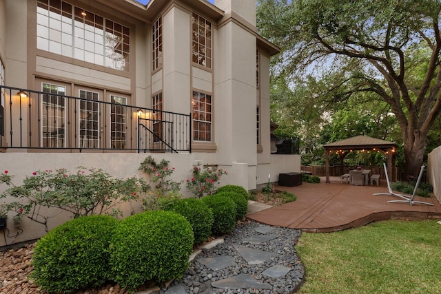 view of property exterior with a gazebo, stucco siding, a deck, and fence
