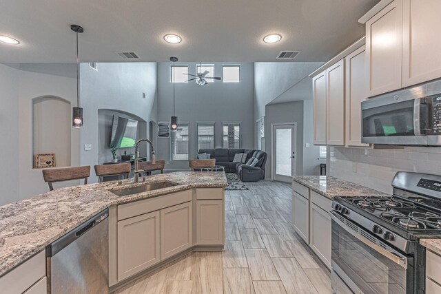 kitchen featuring light stone countertops, appliances with stainless steel finishes, a sink, a ceiling fan, and decorative backsplash