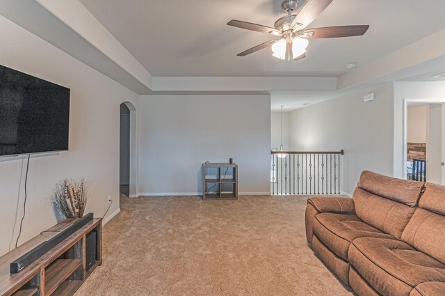 living area featuring carpet flooring, arched walkways, ceiling fan, and a tray ceiling