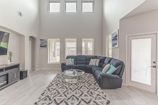 living room featuring arched walkways, a high ceiling, visible vents, and baseboards