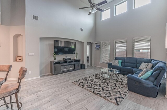 living area with visible vents, a ceiling fan, a towering ceiling, and arched walkways