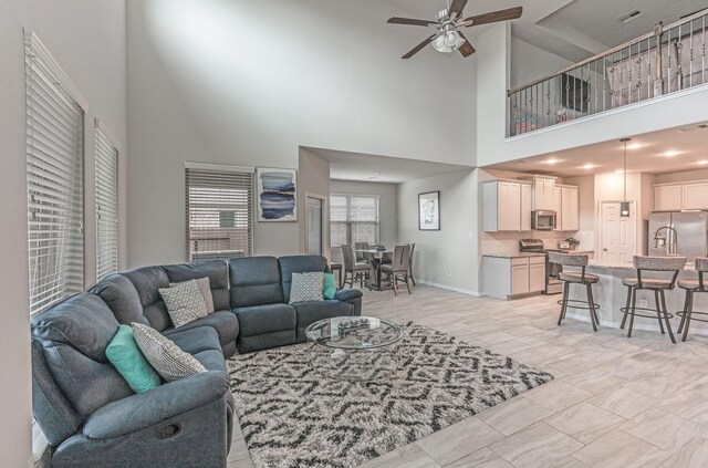 living room featuring baseboards, a high ceiling, ceiling fan, and visible vents