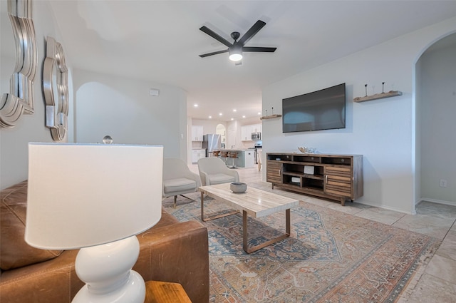 living area featuring arched walkways, ceiling fan, and baseboards