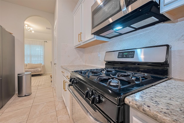 kitchen featuring white cabinets, light stone counters, arched walkways, stainless steel appliances, and backsplash