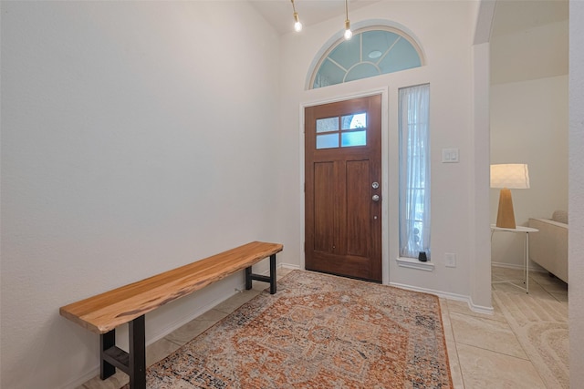 foyer entrance featuring baseboards, light tile patterned floors, and high vaulted ceiling