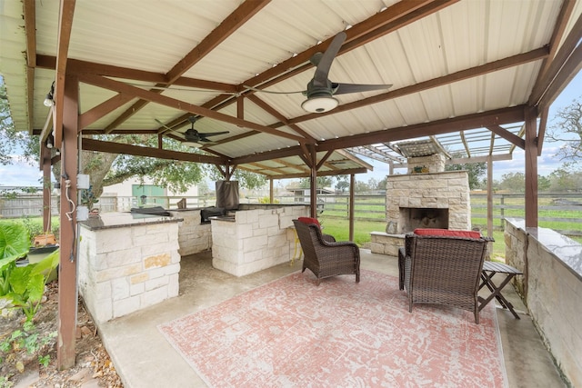 view of patio / terrace with an outdoor stone fireplace, a fenced backyard, ceiling fan, and exterior kitchen